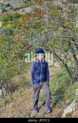 Tired and unhappy boy under the wild rose Bush in the mountains. Crimea Stock Photo