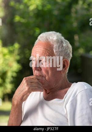 Portrait of old thoughtful man in park with green background. Senior care and depression concept Stock Photo