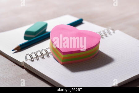Heart shaped stickers on blank note book with pencil and eraser in background, on wooden desk Stock Photo