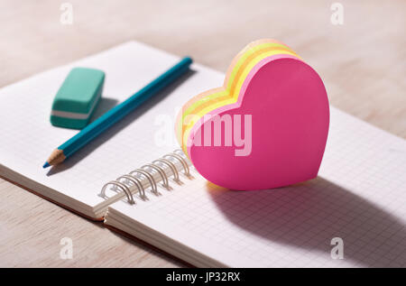 Heart shaped blank stickers on note book with pencil and eraser in background, on wooden desk. Place for your text Stock Photo