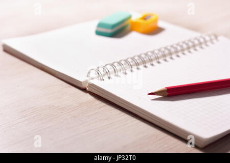 Close up of pencil on blank note book with eraser and sharpener in background on wooden desk Stock Photo