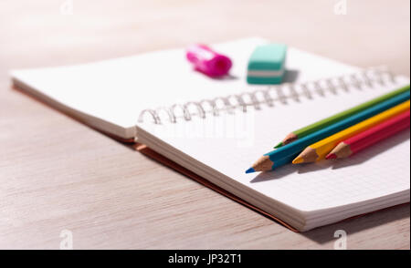 Close up of wooden crayons and other school supplies on blank note book on wooden desk Stock Photo