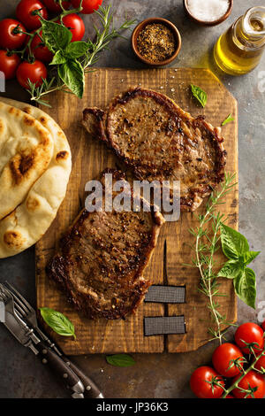 Grilled ribeye steaks with herbs and spices on a wooden board Stock Photo