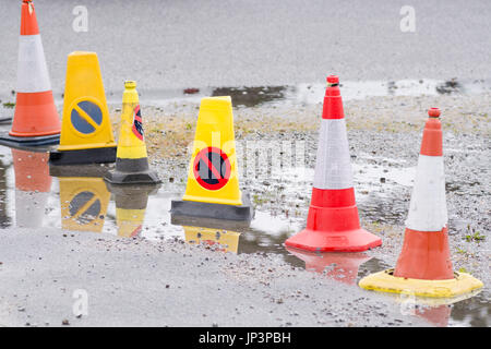 Series of road traffic cones road cones around a pot-holed space in a car park. Possible poor workmanship metaphor. Empty car parking space. Stock Photo
