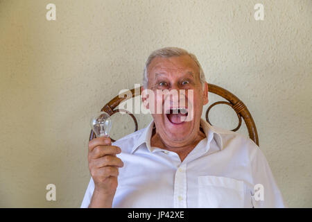 emotional old man holding a light bulb and thinking and finding solution to problem Stock Photo