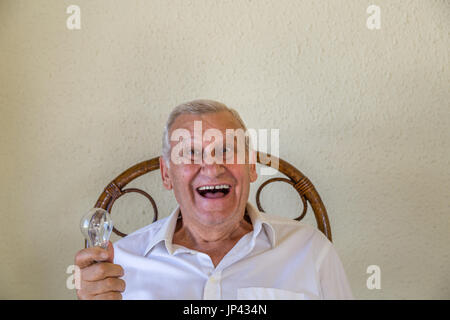 Excited elderly man isolated on yellow wall background  holding bulb meaning idea and innovation concept Stock Photo