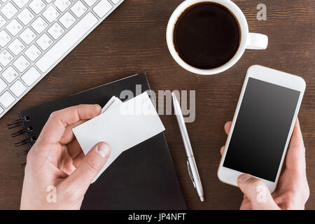 top view of hands holding smartphone and blank cards at workplace Stock Photo