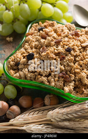 Healthy granola muesli breakfast with grape, nuts and wheat ears in green glass bowl, close up Stock Photo