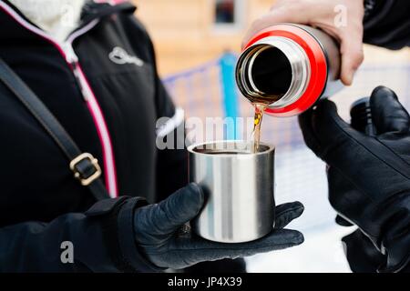 Man pouring hot tea from a thermos into a metal mug Stock Photo