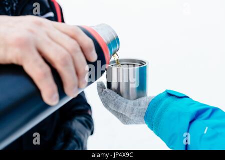 Man pouring hot tea from a thermos into a metal mug Stock Photo