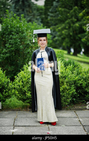 Portrait of a beautiful female graduate in dress and graduation gown with hat posing in the park Stock Photo Alamy