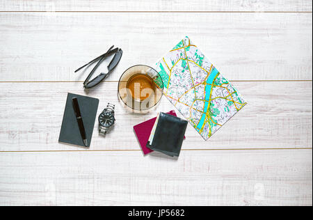 View of a wooden table with a map, watch, passport, notebook, pen, wallet, sunglasses and a cup of coffee on it Stock Photo