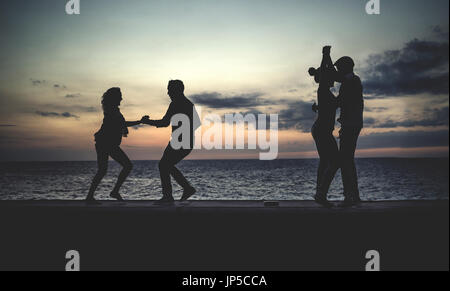 Four people dancing on a sea wall in front of the ocean at dusk. Stock Photo
