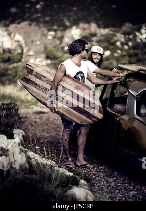 Two young men standing next to car, carrying surfboard. Stock Photo