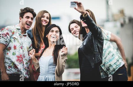 A group of five young people standing on a rooftop posing for a selfie. Stock Photo