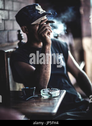 Man sitting at a table in a bar smoking a cigar. Stock Photo
