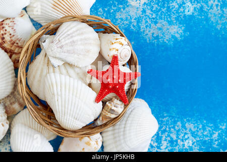 Various seashells in woven basket on blue rustic background. Top view with copy space Stock Photo