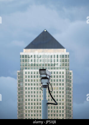 Canary Wharf, a major financial district in London, is seen from across the River Thames with a CCTV camera in the foreground. Stock Photo