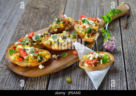 Warm vegetarian canapes: Baked crostini with mixed Greek vegetables with feta cheese served on a wooden cutting board Stock Photo