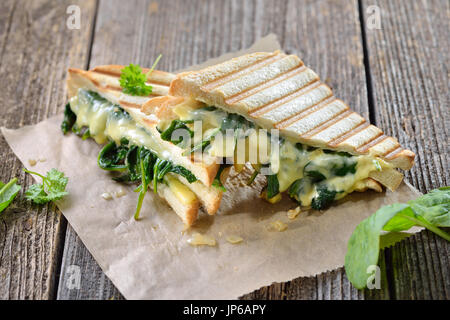 Vegetarian pressed double panini with young spinach leaves, onions and cheese served on sandwich paper on a wooden table Stock Photo