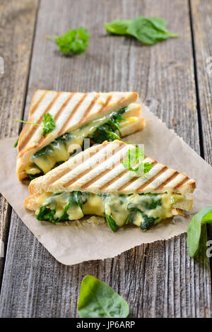 Vegetarian pressed double panini with young spinach leaves, onions and cheese served on sandwich paper on a wooden table Stock Photo