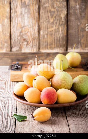Ripe organic apricots and pears in ceramic bowl on rustic wooden table, Ukrainian typical summer fruits Stock Photo