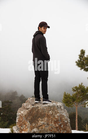 Handsome caucasian young man climbed up a rock in the mountain on a snowy day with foggy background - freedom, joy, goals, positivity, sport concept Stock Photo