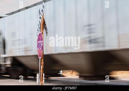 Railcars carrying bulk freight at a railroad crossing marked by a stopsign and RR warning sign. Stock Photo