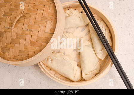 Dumpling in a Container before Steaming and a Pair of a Black Chopsticks. Dumplings is a type of Dim Sum, a food typical from Hong Kong and Canton are Stock Photo