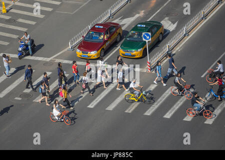 Pedestrians, cyclists and moped crossing street across a crosswalk while taxis wait Stock Photo