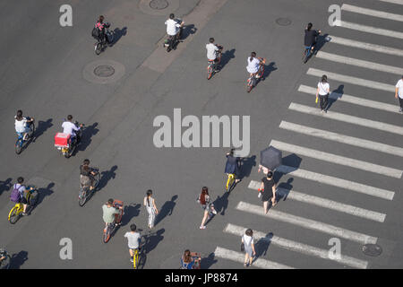 Pedestrians, cyclists and moped crossing street across a crosswalk while taxis wait walking across a wide city street with crosswalk Stock Photo