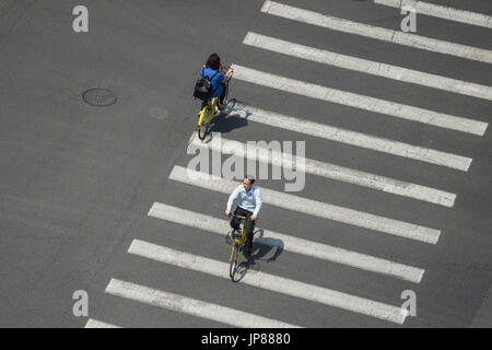 Aerial view of two people bicycling across the crosswalk of a wide road casting shadows on the lines Stock Photo