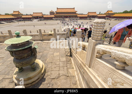 Tourists holding shade umbrellas walking from Meridian Gate passing by inense urn in Foribdden City Stock Photo