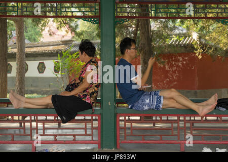 Two Chinese tourists taking a break while visiting the Summer Palace sitting on the railing of the Long Corridor Stock Photo