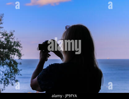 Woman with long hair taking photos of the sea below after sunset Stock Photo