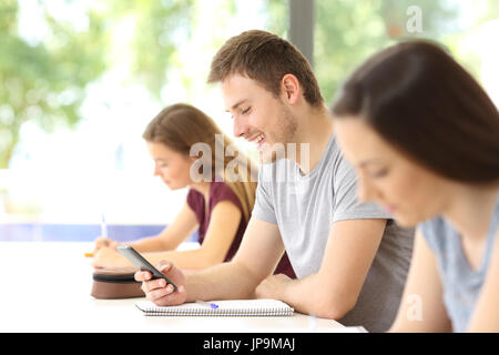 Side view of a student distracted with a mobile phone during a class at classroom Stock Photo
