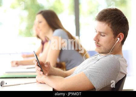 Bad student distracted listening to music sitting in a classroom Stock Photo