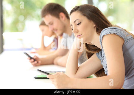 Side view of three bad students distracted using smart phones during a class in a classroom Stock Photo