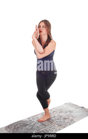 A slim young woman in an exercising outfit standing on a gray towel on  one leg with her legs and arms twisted, isolated for white background Stock Photo
