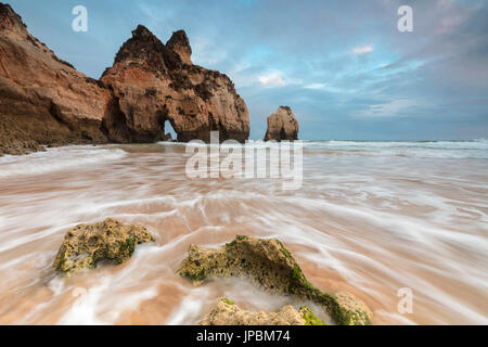 Clouds frame the rough sea and cliffs at sunset Praia Dos Tres Irmaos Portimao Algarve Portugal Europe Stock Photo
