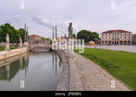 View of the Prato della Valle, Padua, Italy on an overcast day with reflections of the statues in the water of the elliptical canal and an historic building in the background, veneto, italy, europe Stock Photo