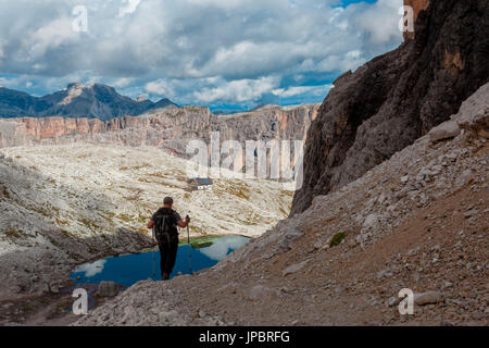 Hikers descending the path SAT 666, at the bottom the turquoise lake Piasciadu and back the Franco Cavazza hut. Dolomites, in the Sella Group. Stock Photo