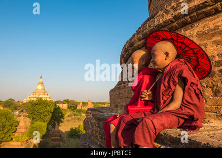 Bagan, Mandalay region, Myanmar (Burma). Two young monks sitting on top of a stupa with the Shwesandaw pagoda in the background.