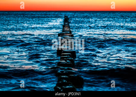 Wooden groynes with blue water and red sunset. Stock Photo