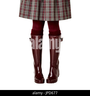 Female legs in a skirt in a cage, in burgundy pantyhose and in crimson rubber boots on an isolated background. Selective focus. Stock Photo