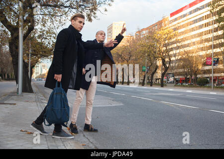Two young handsome caucasian businessmen outdoor in the city asking for a taxi. Stock Photo