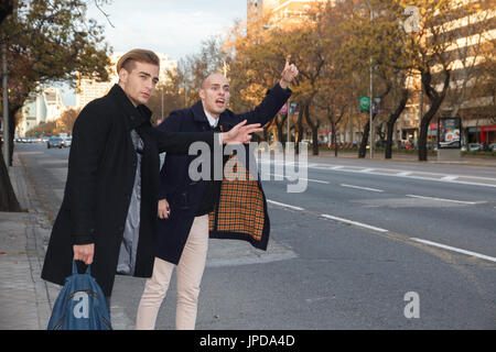 Two young handsome caucasian businessmen outdoor in the city asking for a taxi. Stock Photo