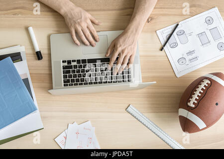 Man is using a laptop on the wooden table in the workshop. Around the laptop there are draughts, drafts, notebook and books, marker and a pencil, rule Stock Photo