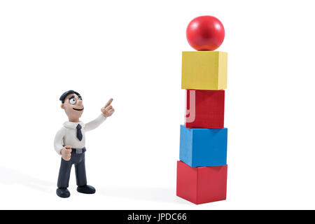 Plasticine businessman points to a toy tower from wooden blocks with the ball at the top isolated on white background Stock Photo