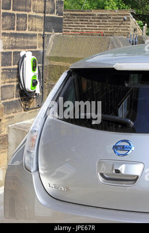 All electric Nissan Leaf car and charging station outside private house.